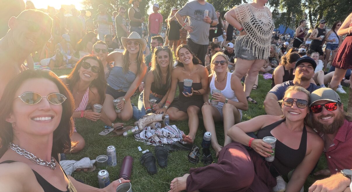 Friends gathered on the grass at a sunlit festival, smiling together