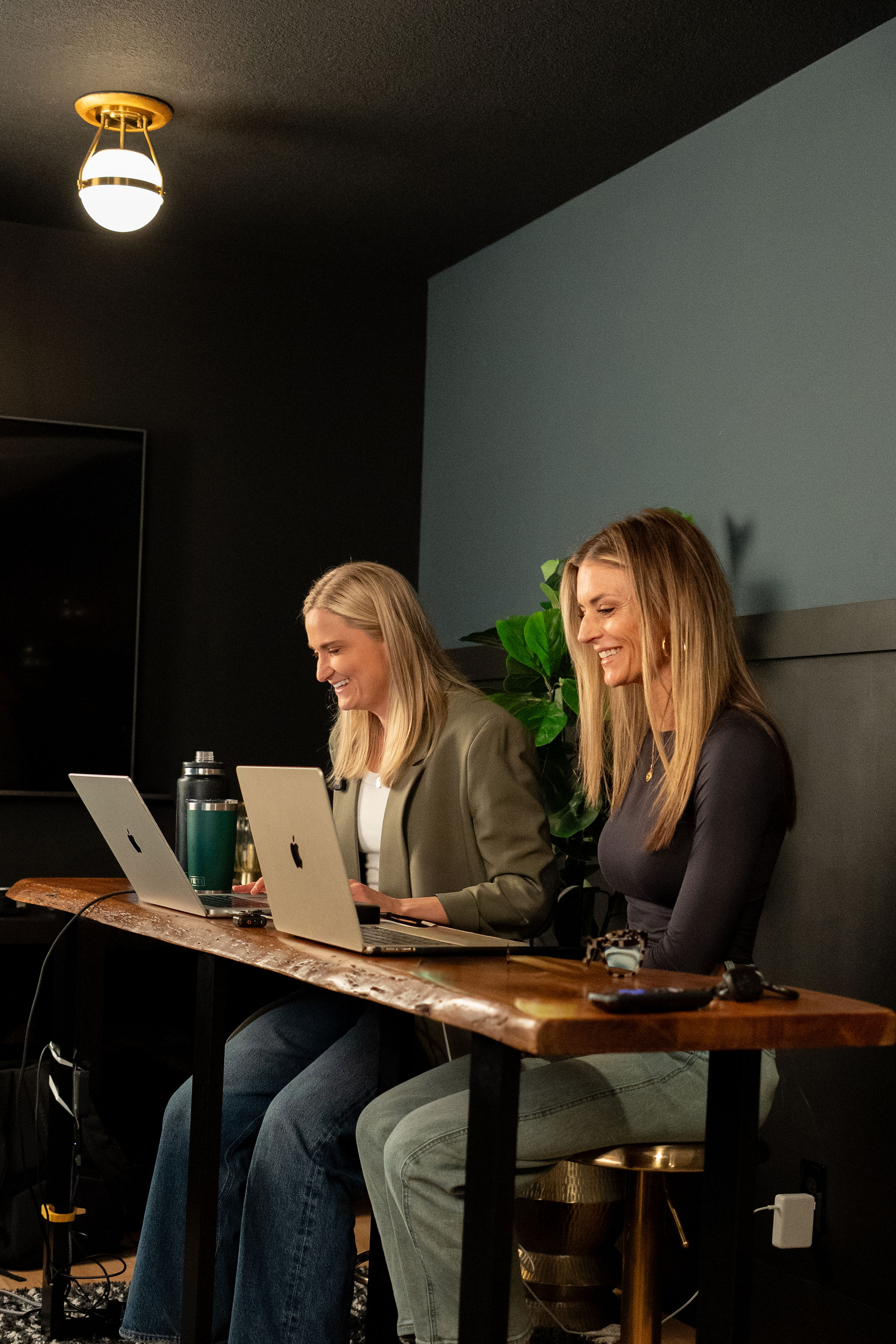 Kinsey and Callan side by side at a long wood desk, both smiling at their laptops