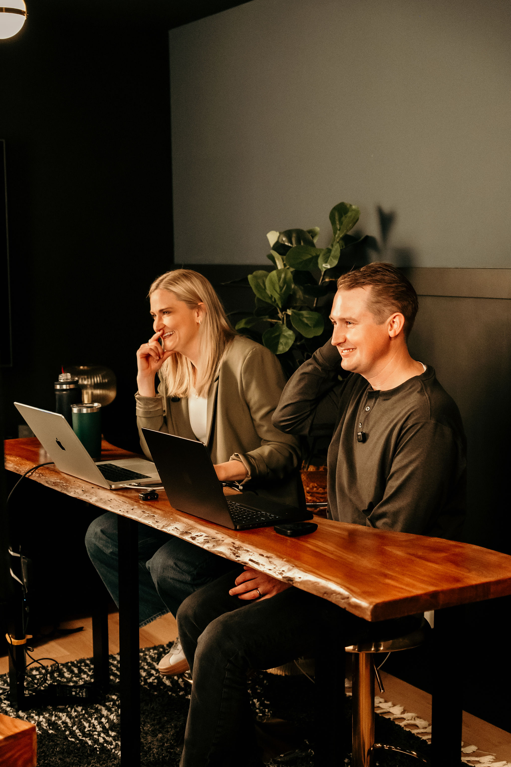 Two teammates smiling at their laptops at a live-edge wood desk