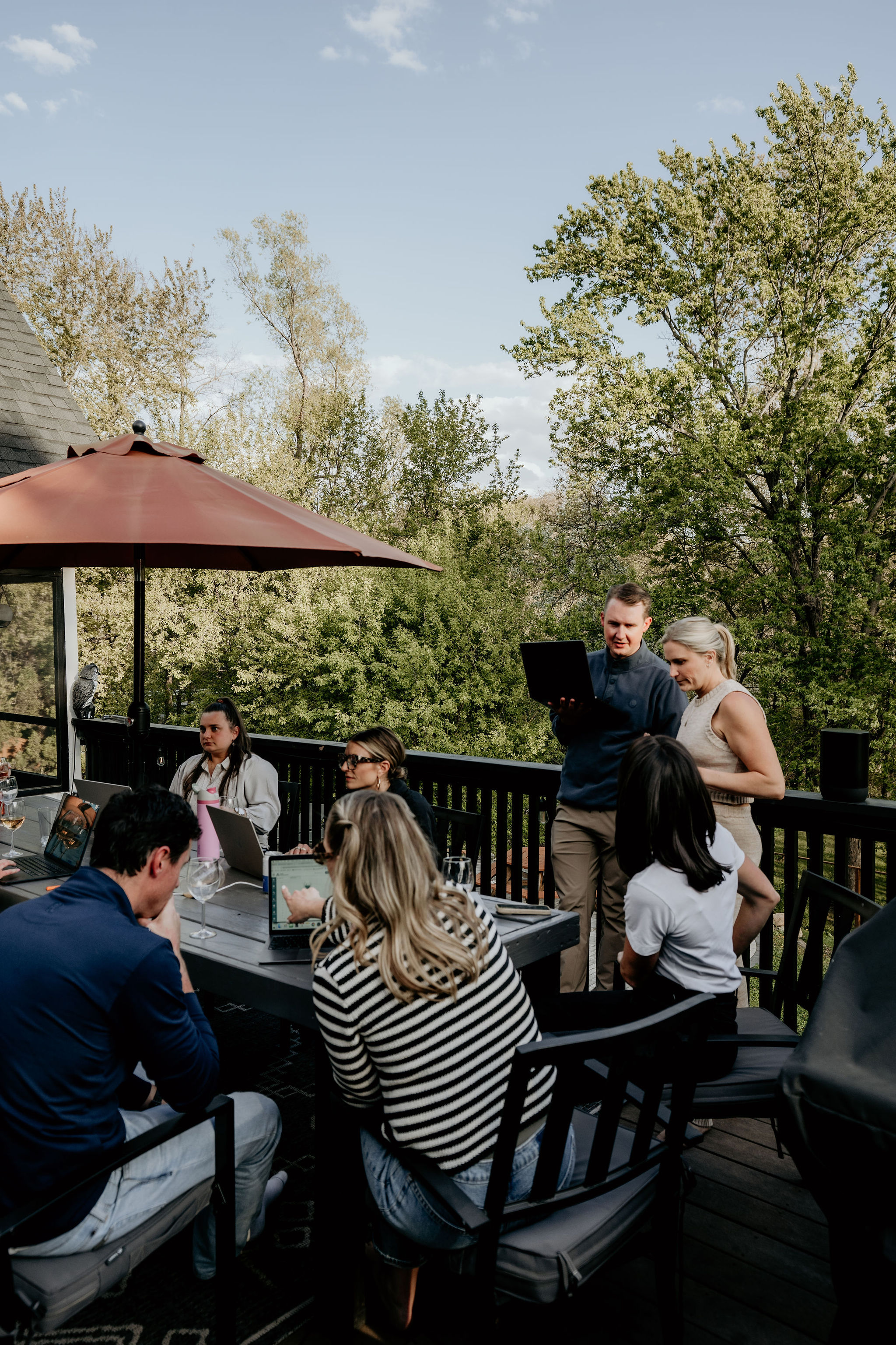 The team gathered around a table on a sunny deck, laptops open