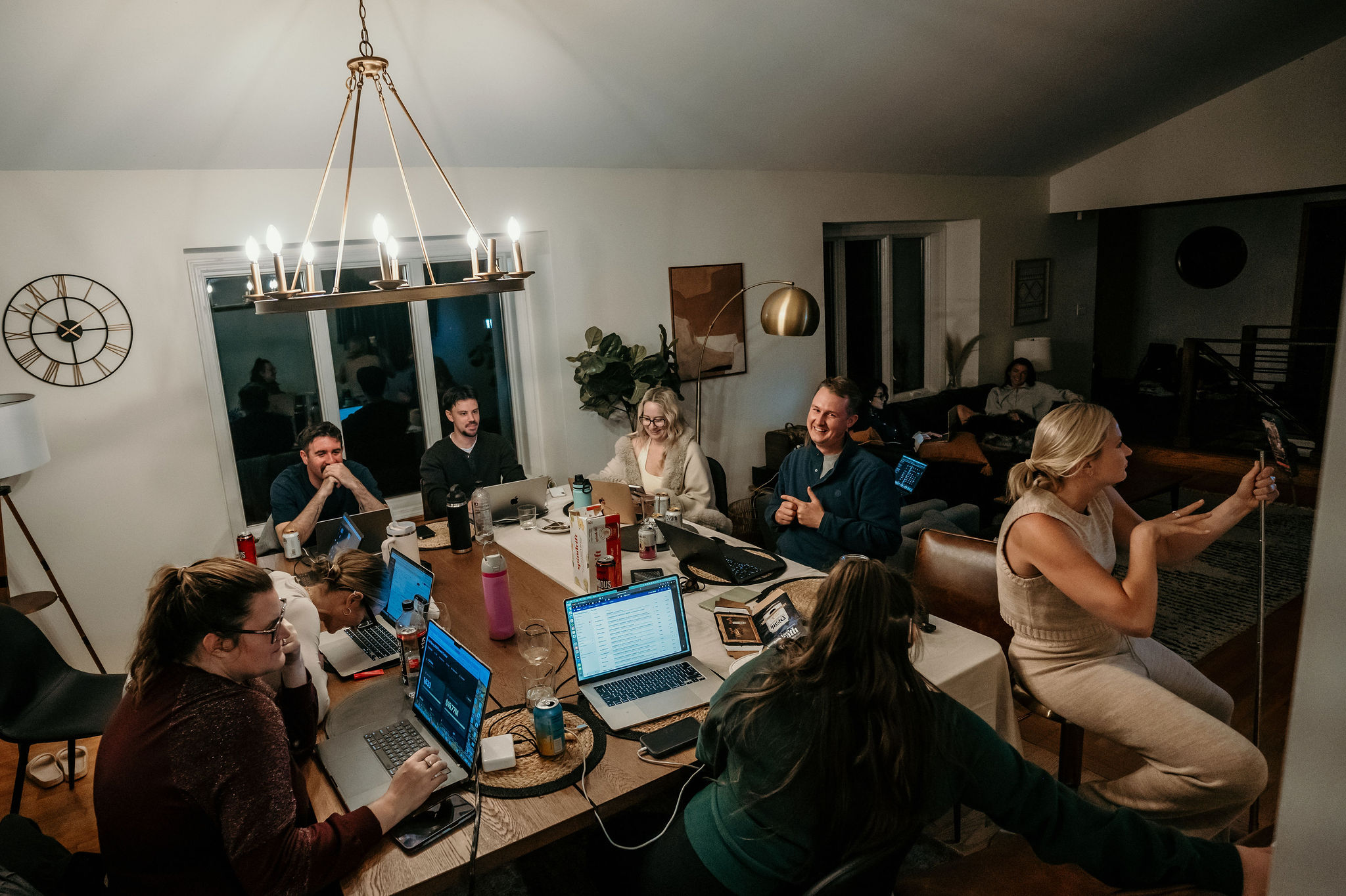 The whole room together at night, laptops open under the chandelier